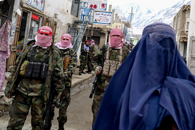 Taliban security personnel stand guard as an Afghan burqa-clad woman walks along a street at a market.