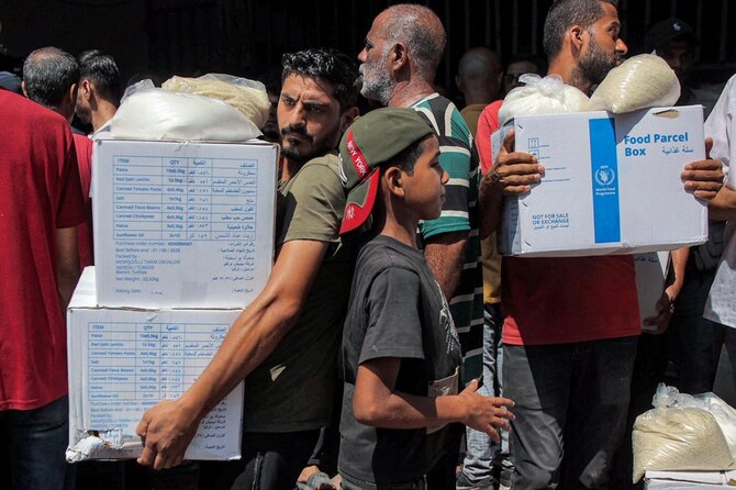 People receive humanitarian aid packages provided by UNRWA from a warehouse in central Gaza City on August 27, 2024. (AFP)